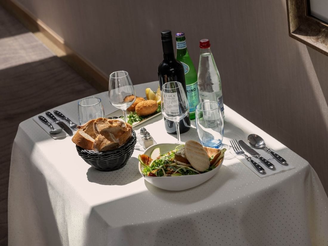Table setting for one with bread in a basket placed by a salad near wine bottles at Warwick Grand Place Brussels