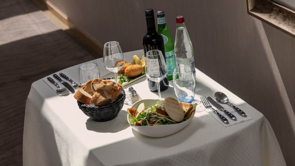 Table setting for one with bread in a basket placed by a salad near wine bottles at Warwick Grand Place Brussels