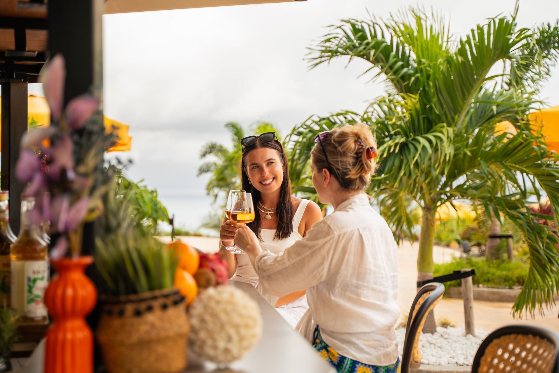Twee vrouwen proosten met drankjes in een buitenomgeving, omringd door groene planten in Pool Bar bij Golden Rock Resort