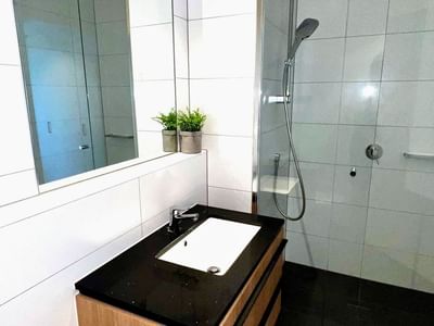 Modern bathroom with a white sink, black countertop, and glass shower at Zamia Apartments.