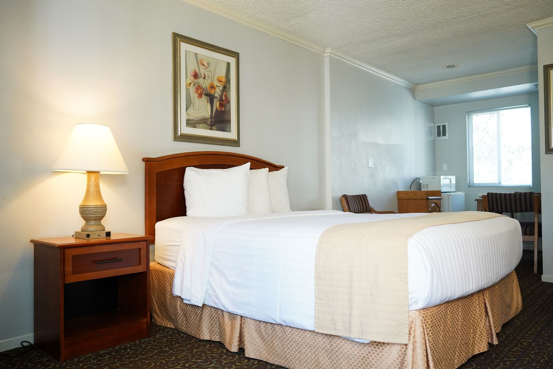 A standard hotel room with a bed, nightstand, lamp, and artwork on the wall.