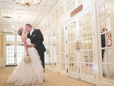 Bride and groom kissing near French doors outside Laurel Ballroom A with mirrored reflections at The Simsbury Inn