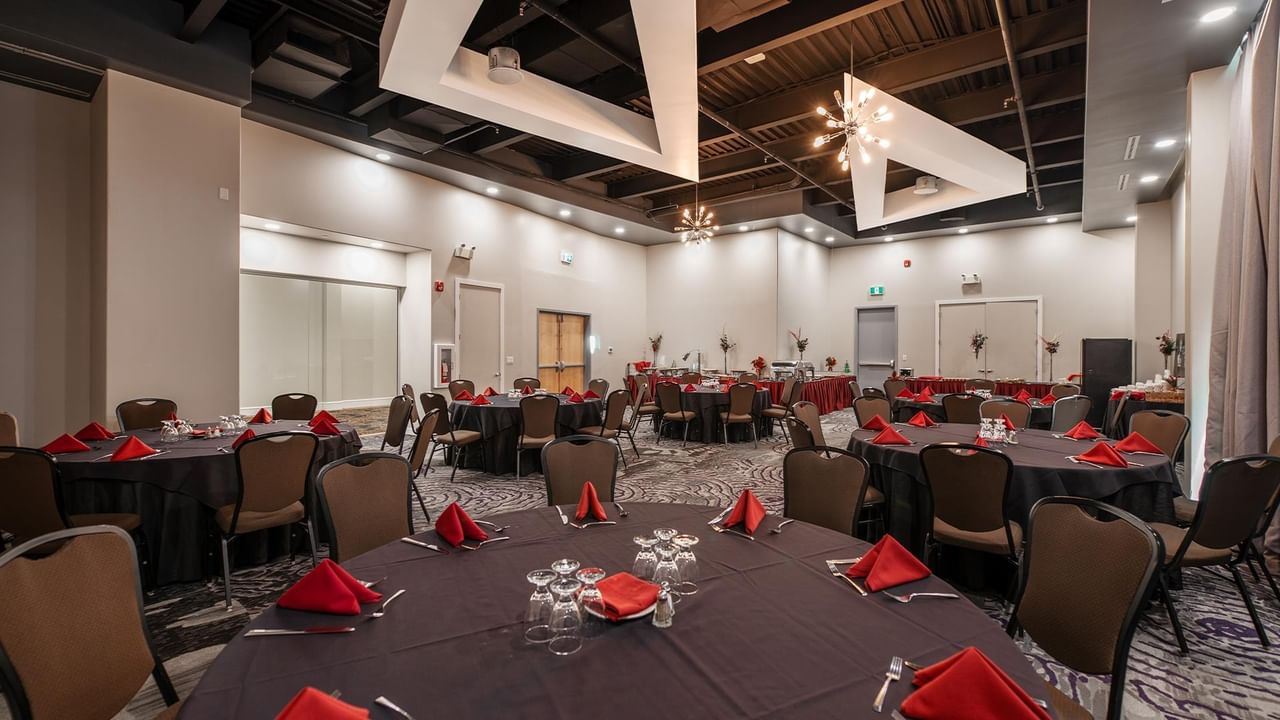 Elegantly set dining tables with red napkins and glasses in an event space.