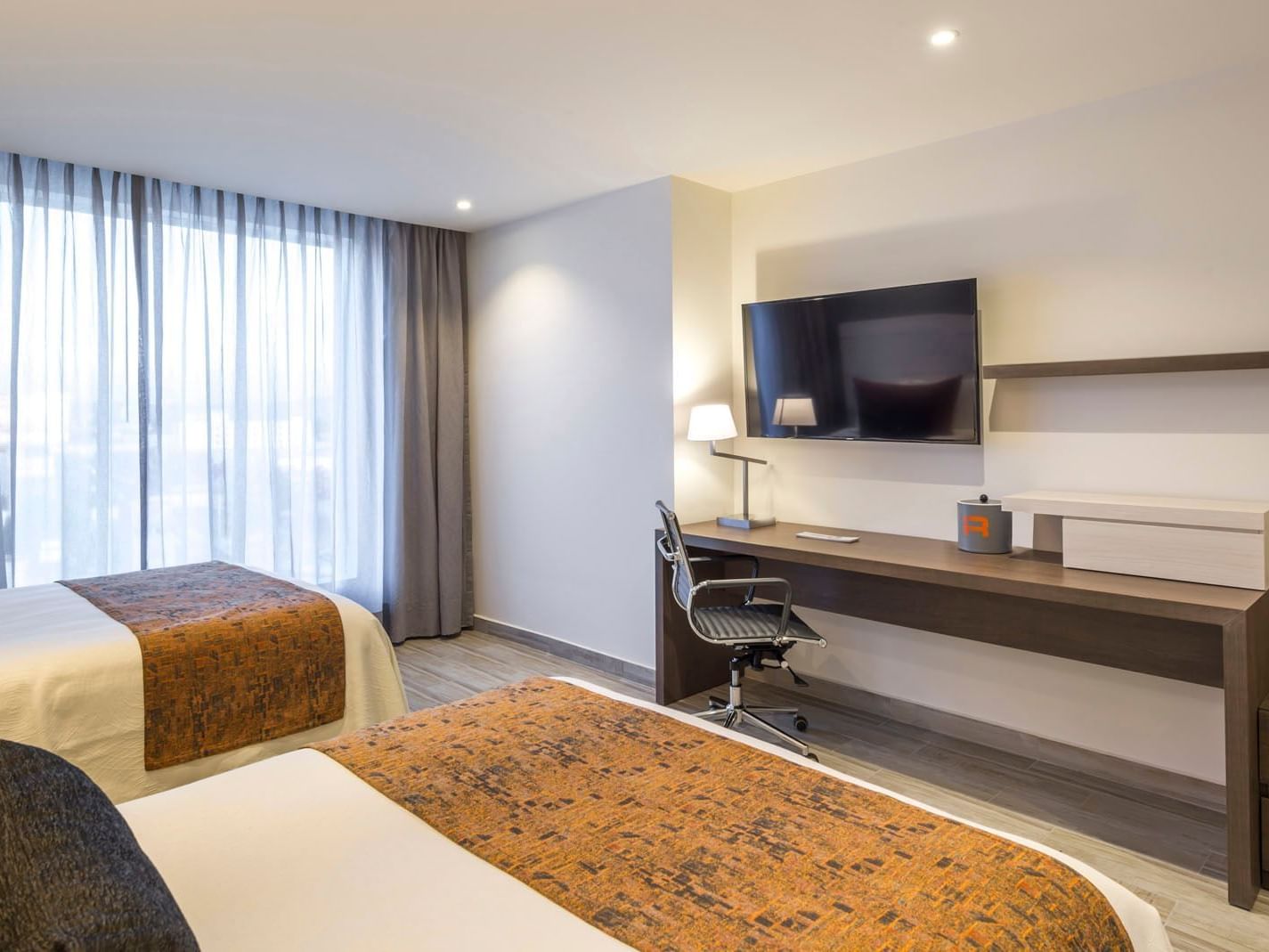 2 Double Deluxe room featuring two beds, a workspace with a lamp, and large windows with shears at Real Inn Celaya