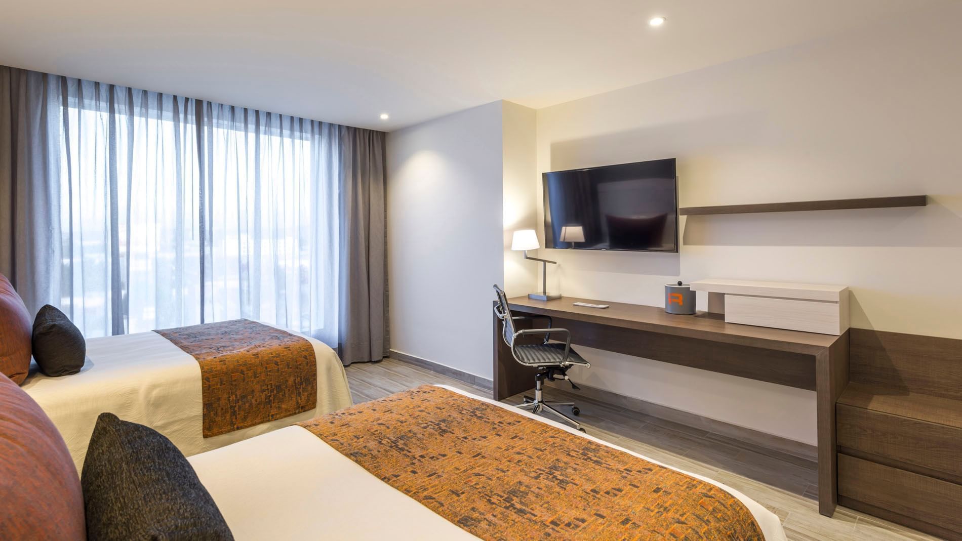 2 Double Deluxe room featuring two beds, a workspace with a lamp, and large windows with shears at Real Inn Celaya