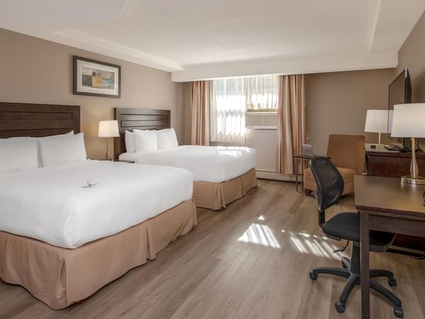 Two queen beds, a desk, and a chair in a hotel room