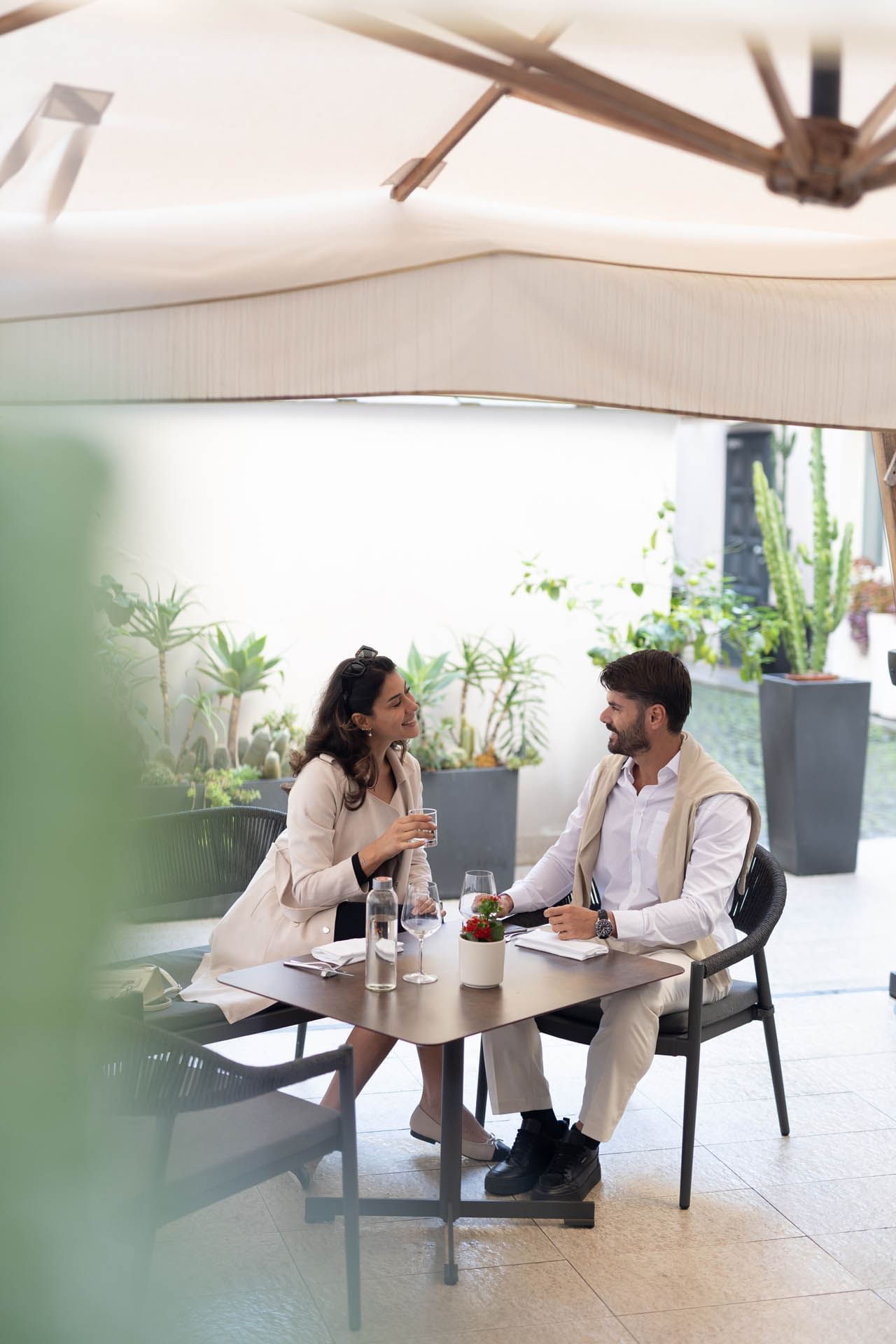 A couple enjoys drinks at a stylish outdoor restaurant with lush greenery and modern decor at The Guardian Hotel