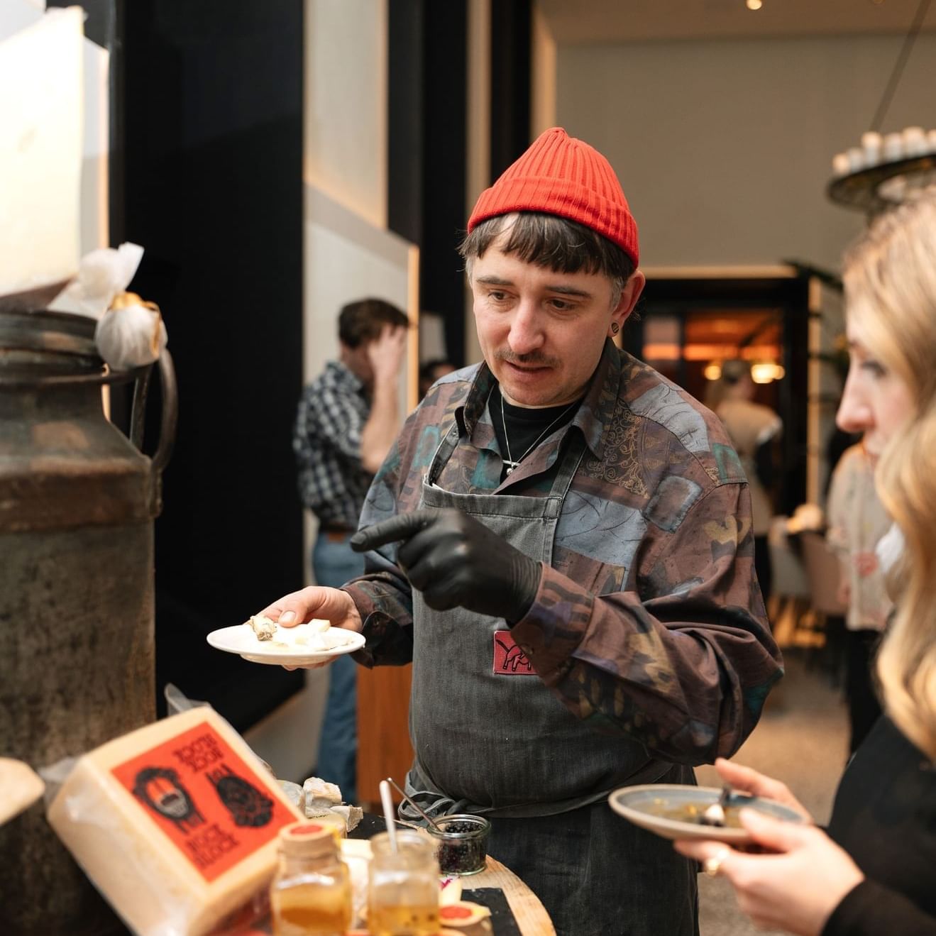Vendor offering food as customer samples from a rustic table of cheese and jars at Almanac Palais Vienna