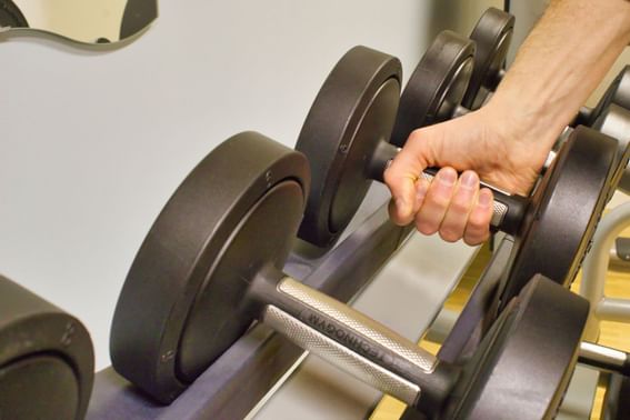 Person grabbing a dumbbell from a rack at Fitness Room in Starling Hotel Lausanne