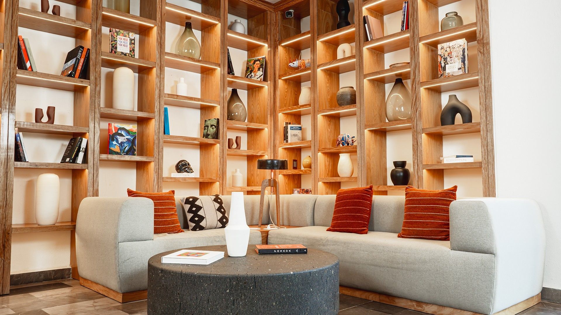 Cozy seating area with orange pillows and backlit shelves in Library Café & Deli at Camino Real Zaashila Huatulco