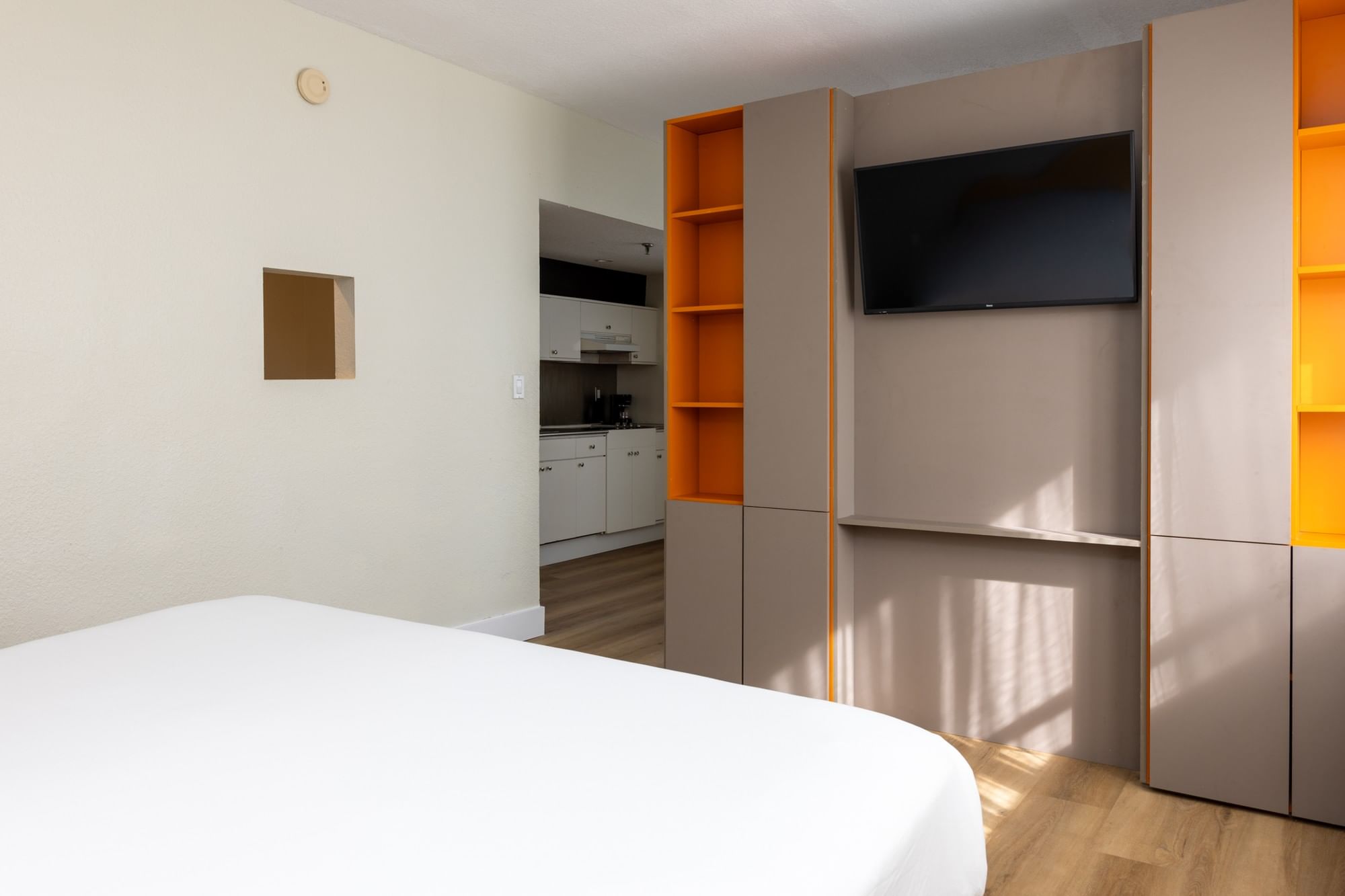 A studio room with a king bed, kitchenette, and flat-screen TV on a wall with built-in shelves and cabinets.