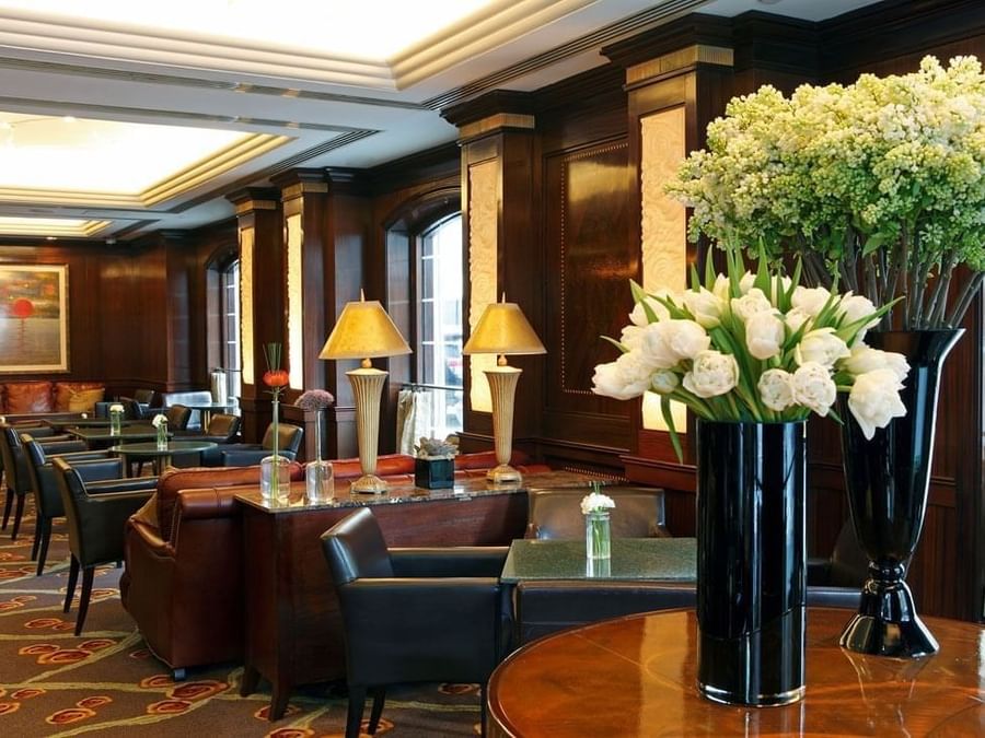 Elegant hotel lobby with dark wood paneling, leather seating, table lamps, and fresh white floral arrangements at Warwick New York