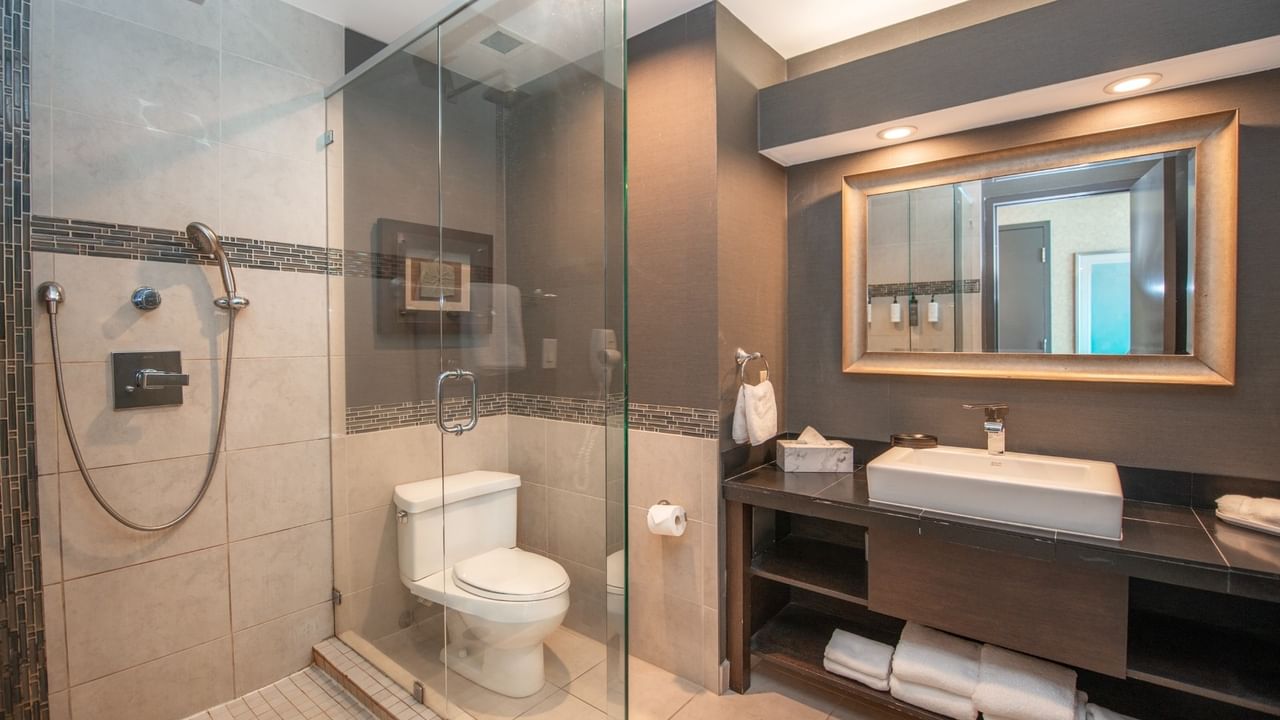 Coast Waterfront Suite bathroom with a glass shower, sink, mirror, and stacked towels at Coast Lonsdale Quay Hotel