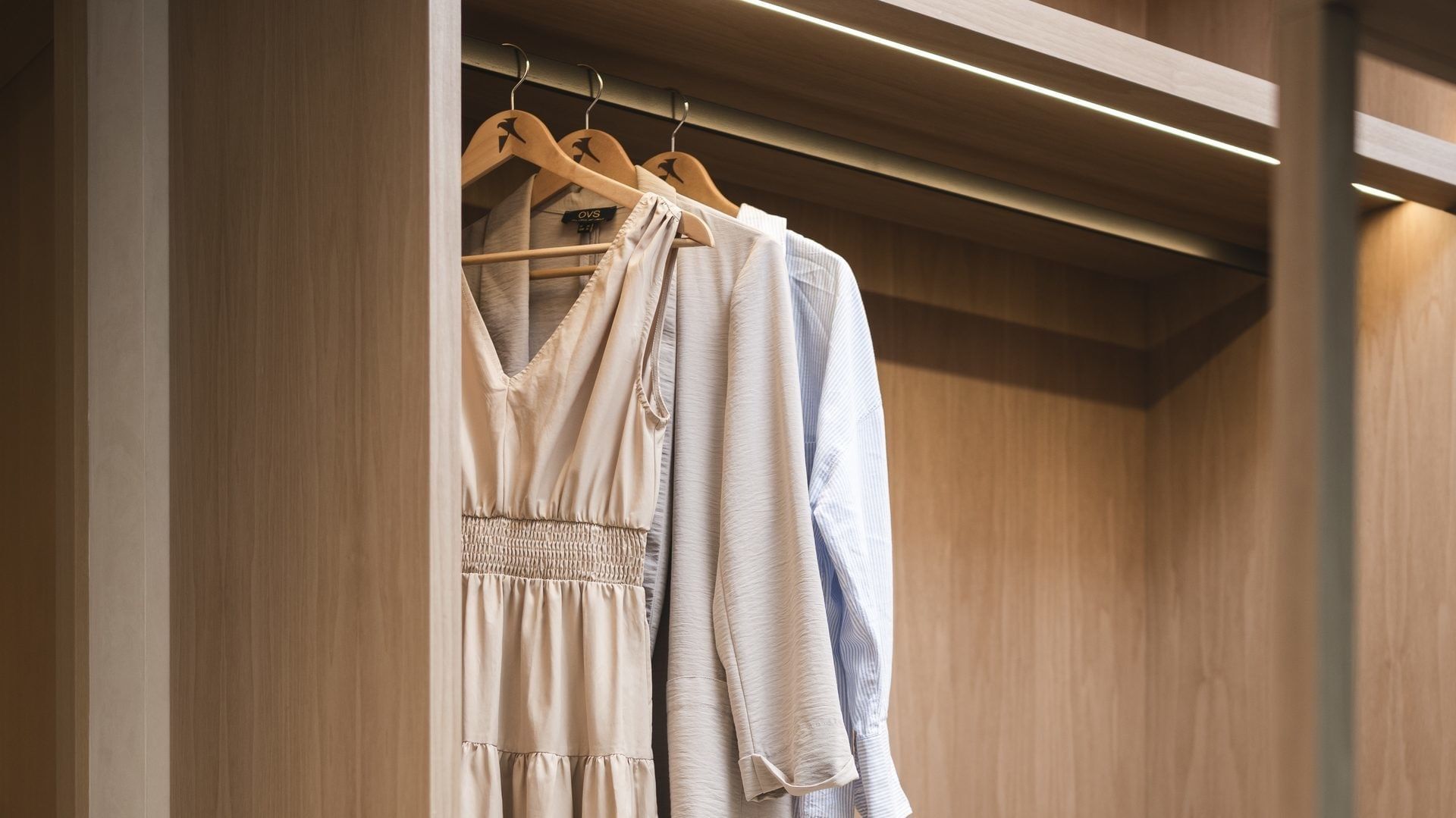 Armadio in legno con due abiti appesi su appendini e luci integrate sul soffitto.