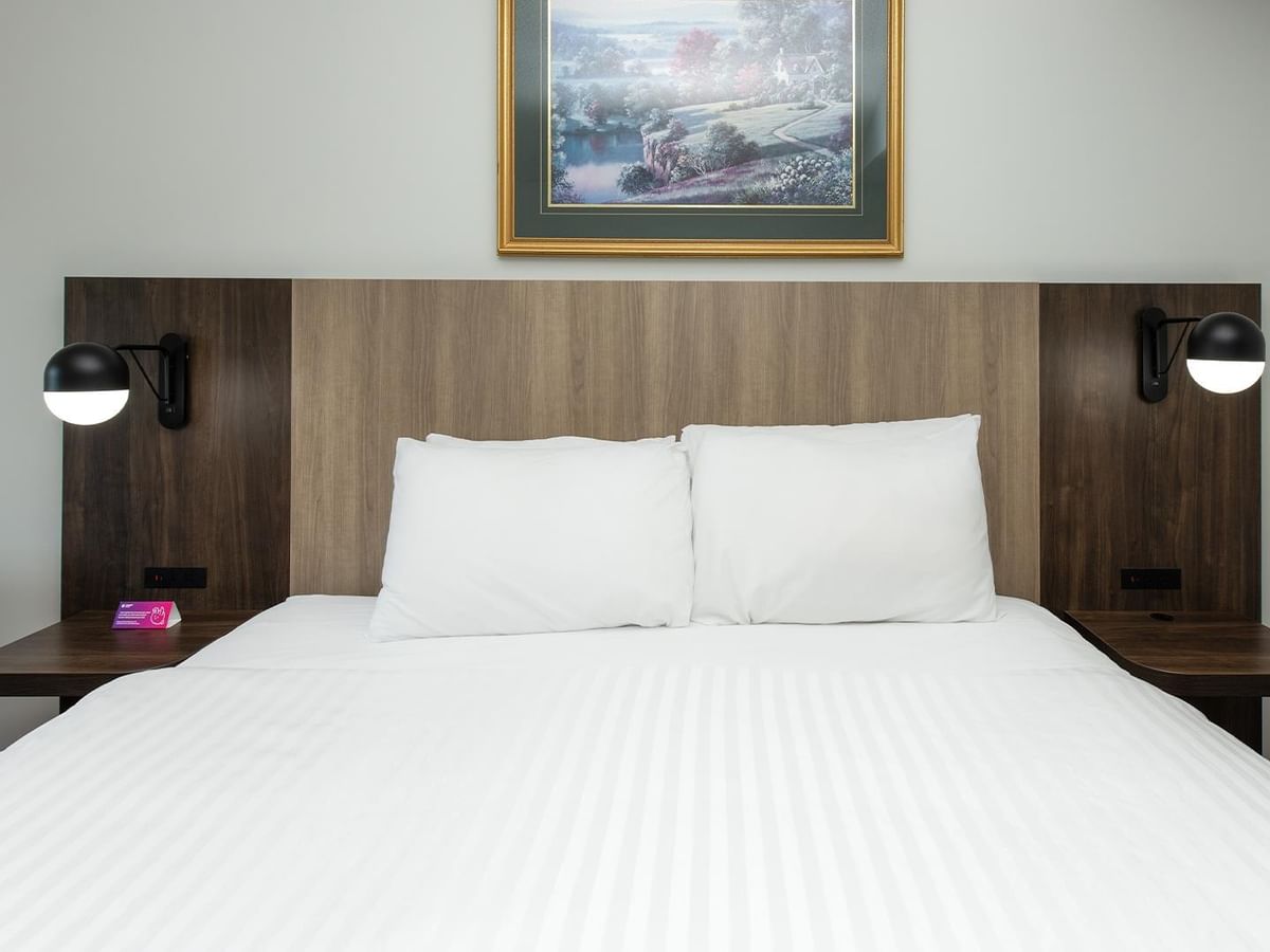 Coast King room with white bedding, wood headboard, and modern sconces.