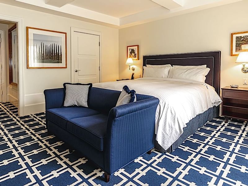Spacious hotel suite at El Prado Hotel, with a comfortable bed, stylish blue sofa, and geometric rug