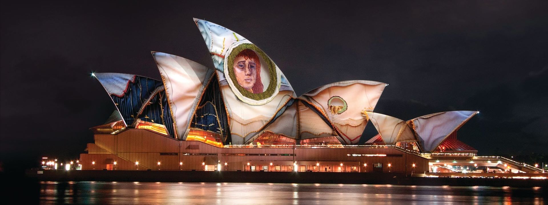 Illuminated Sydney Opera House with a large portrait at night for Vivid Sydney 2026.