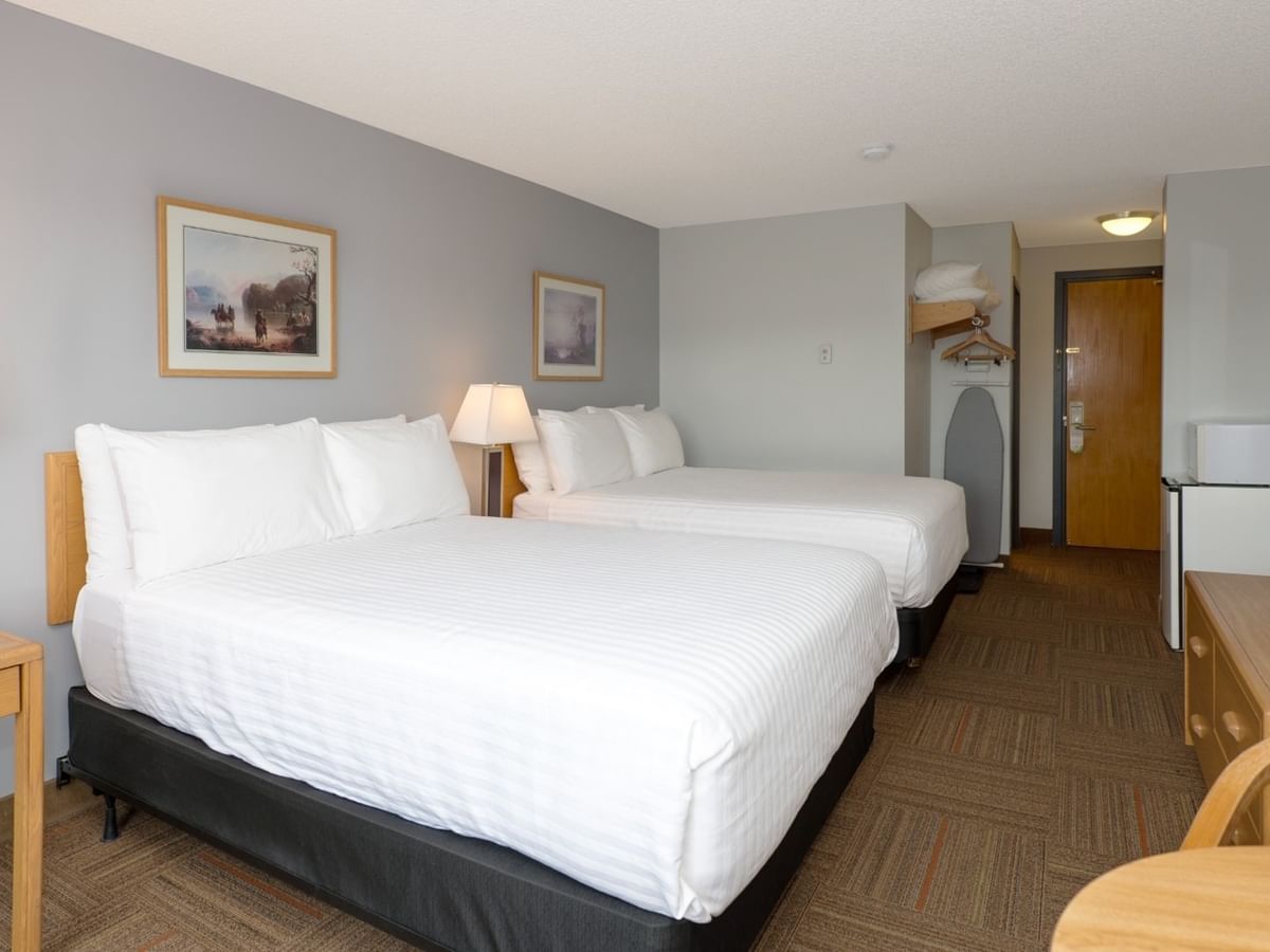 Two beds, nightstands with lamps, TV, and a door in a hotel room.