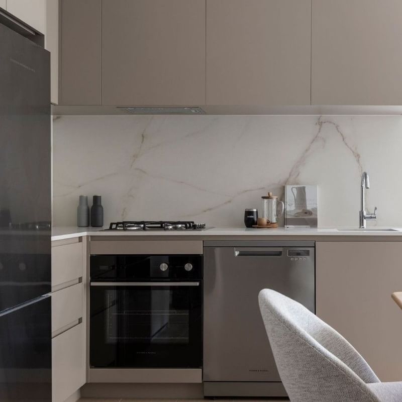Modern kitchen with marble backsplash, stainless steel appliances, and dining area with wooden table and chairs.