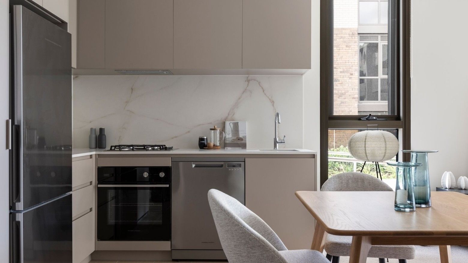 Modern kitchen with marble backsplash, stainless steel appliances, and dining area with wooden table and chairs.