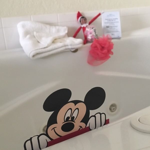 Elf on the shelf sitting on a bathtub edge with a Mickey Mouse graphic at Lake Buena Vista Resort Village & Spa