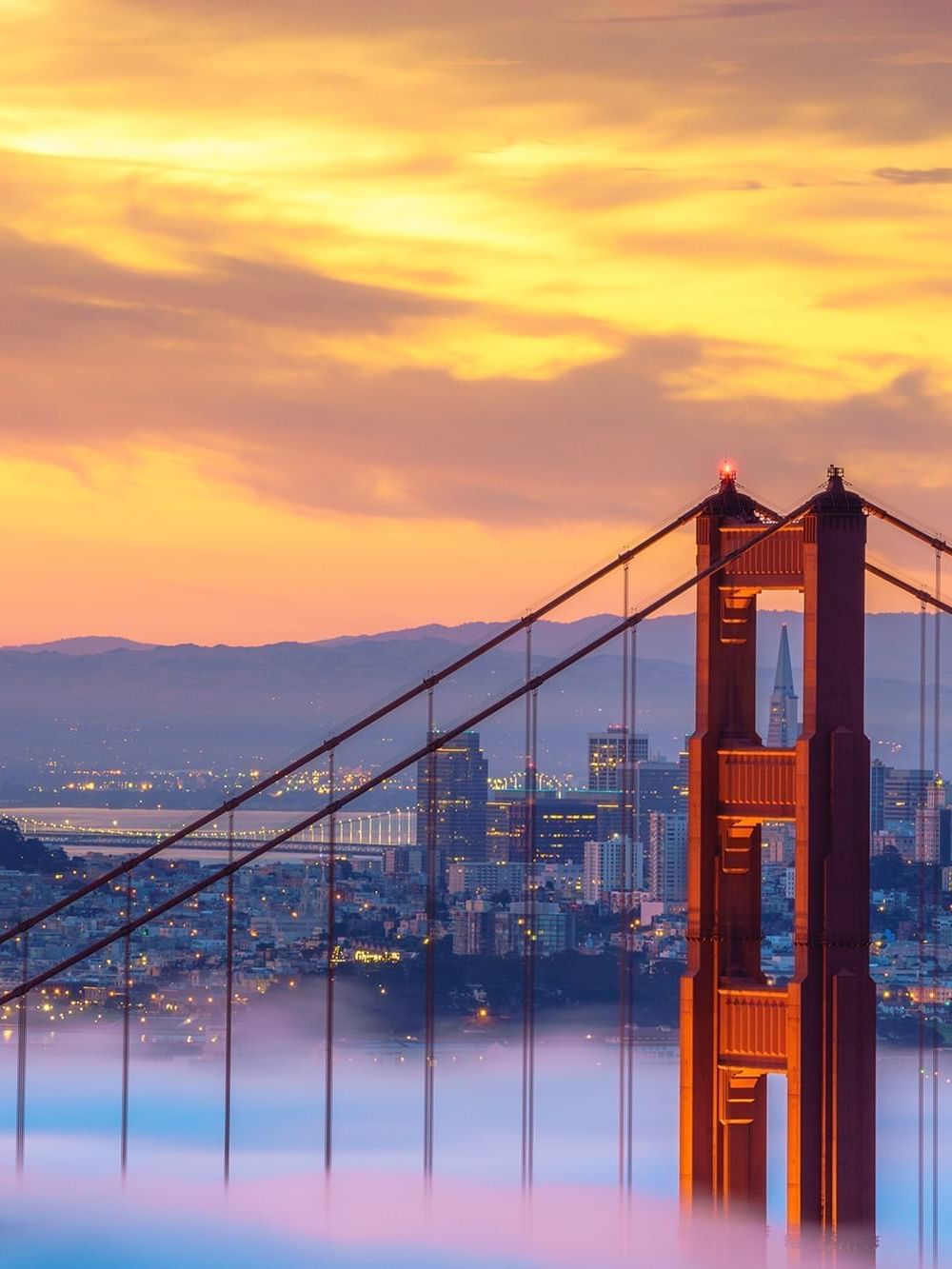 Golden Gate Bridge by a misty city skyline under a vibrant orange sunset near Warwick San Francisco