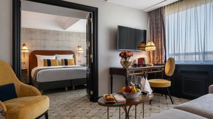 Chambre élégante avec lit, bureau, chaise, corbeille de fruits et télévision à l'hôtel Barsey by Warwick de Bruxelles.