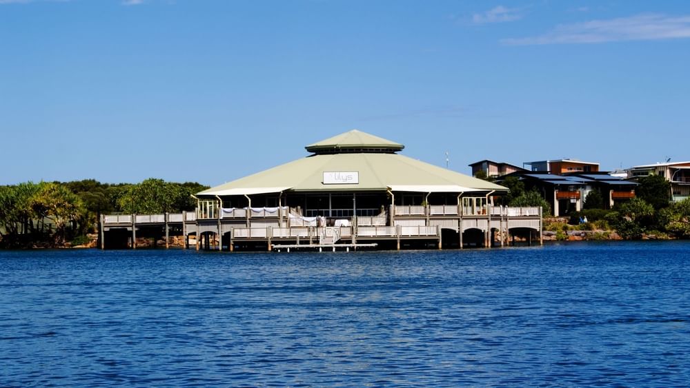 Lily’s on the Lagoon with a green roof stands by the water, surrounded by trees at the Novotel Sunshine Coast Resort