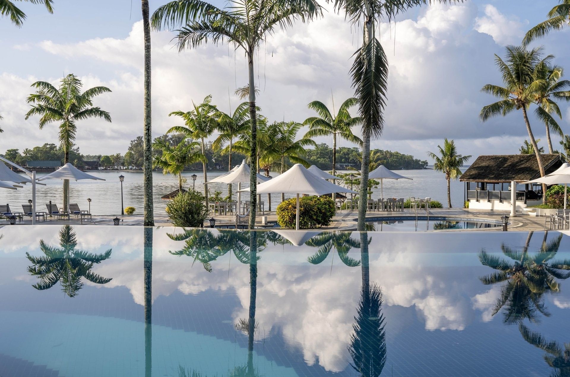 Palm trees and white umbrellas perfectly reflected in the still surface of an infinity pool at Warwick Le Lagon - Vanuatu