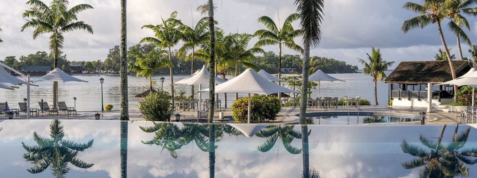Tranquil pool with lush palm trees and a serene beach view at Warwick Le Lagon - Vanuatu, Efate