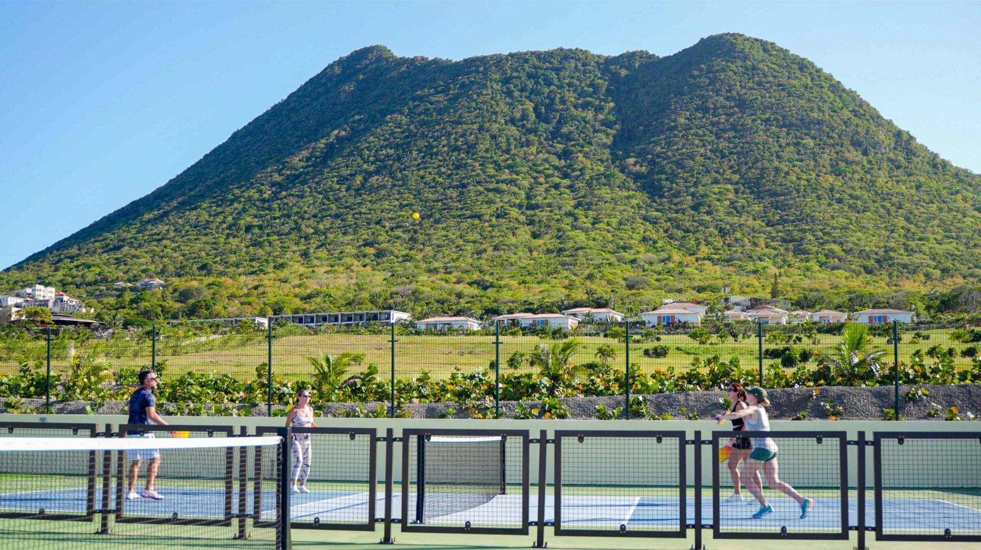 Vier mensen spelen pickleball op een baan met een groene berg op de achtergrond nabij Golden Rock Resort