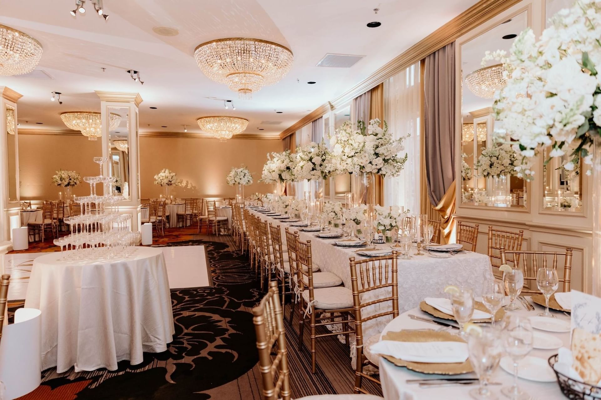 Long banquet table by gold chairs under large crystal chandeliers and tall florals at Warwick Melrose Dallas