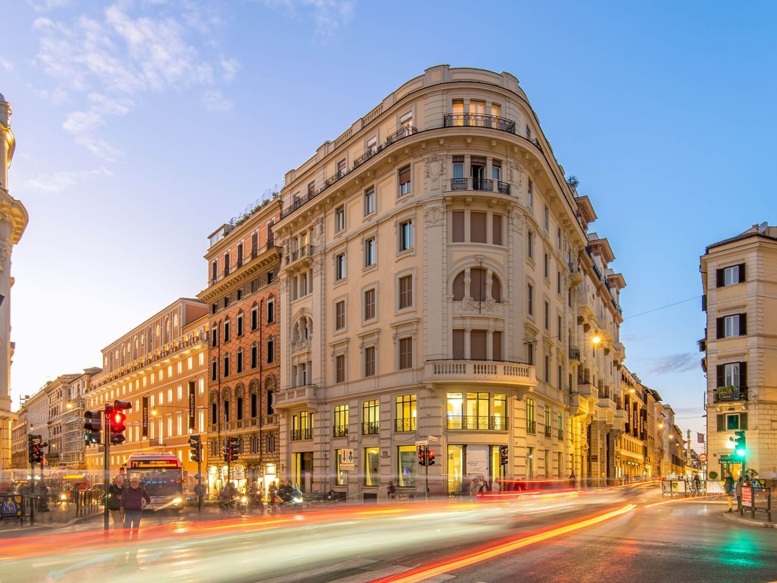 Sunset view of Rome's Via del Tritone, with vibrant light trails from passing vehicles near The Guardian Hotel
