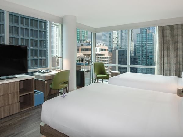 Two beds, TV, desk, and cityscape view in Coast Two Queens Corner Room.