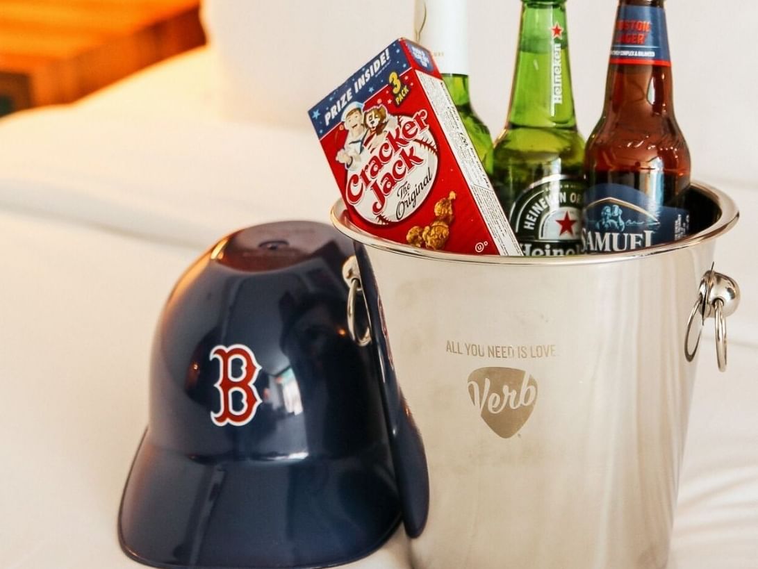 Baseball cap with team logo beside ice bucket filled with beer bottles and Cracker Jack for The BALLPARK Package