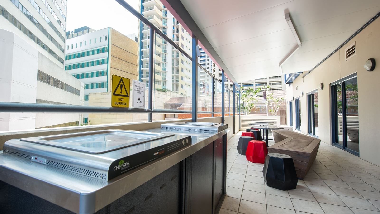 Modern outdoor terrace with stainless steel barbecue grills, colorful seating, and city views at StudentLiving - on Margaret