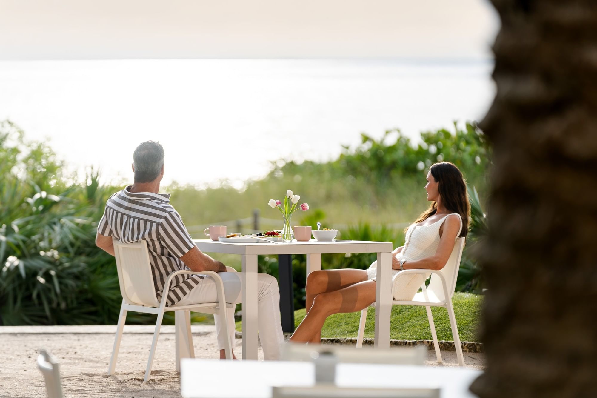 A couple sits at a table on the beach in front of a palm tree.