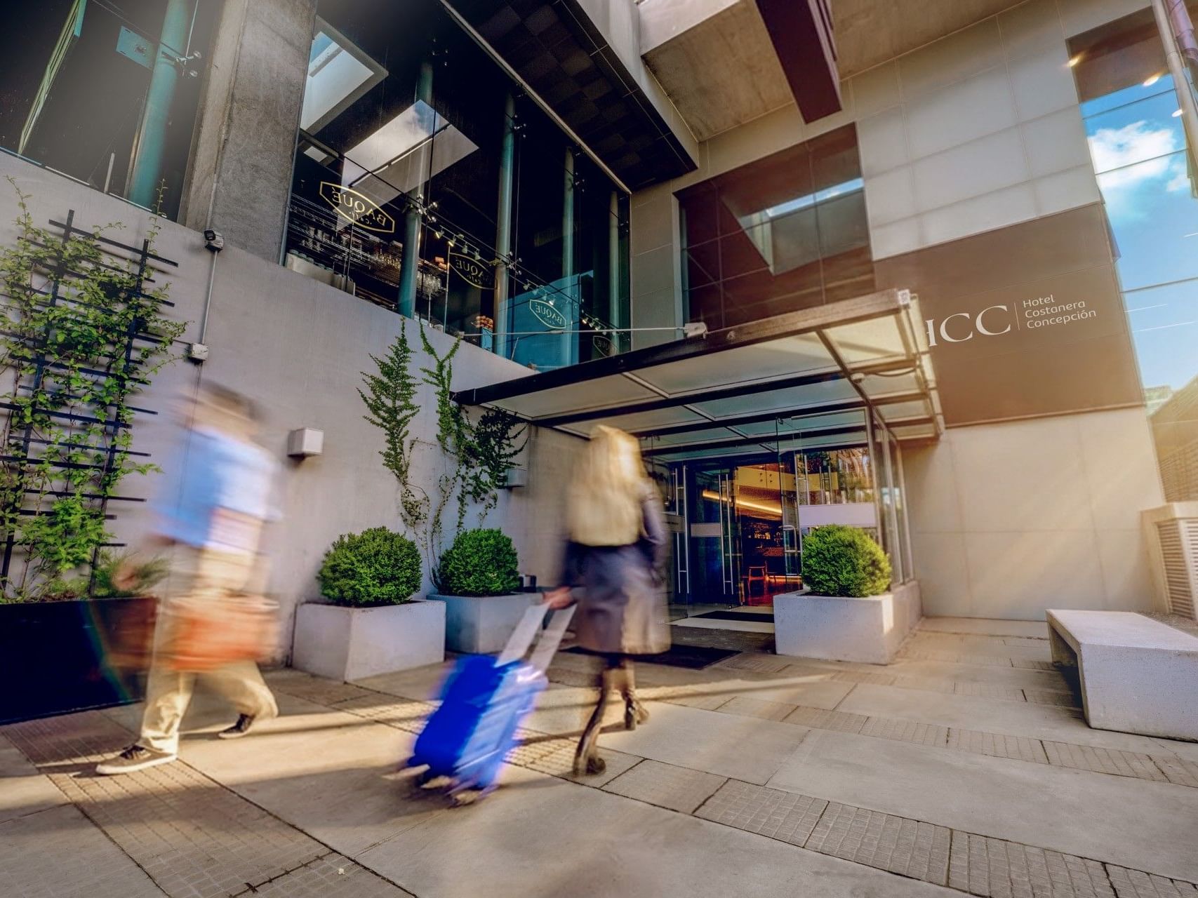 Personas que entran en el HCC Hotel Costanera Concepción con equipaje y una bolsa.