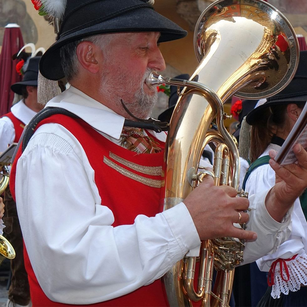 Ein Mann in traditioneller Tracht spielt eine goldene Tuba in einer Gruppe von Musikern.
