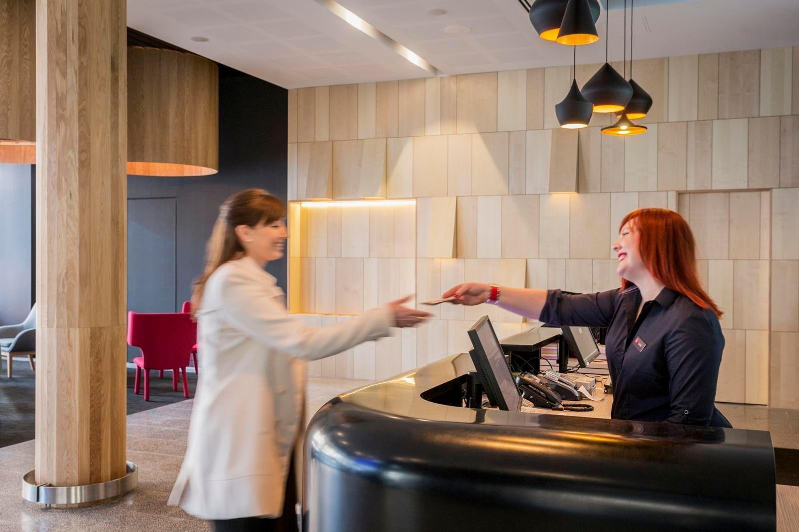 Guest happily receiving a key card from a smiling receptionist at Ibis Adelaide