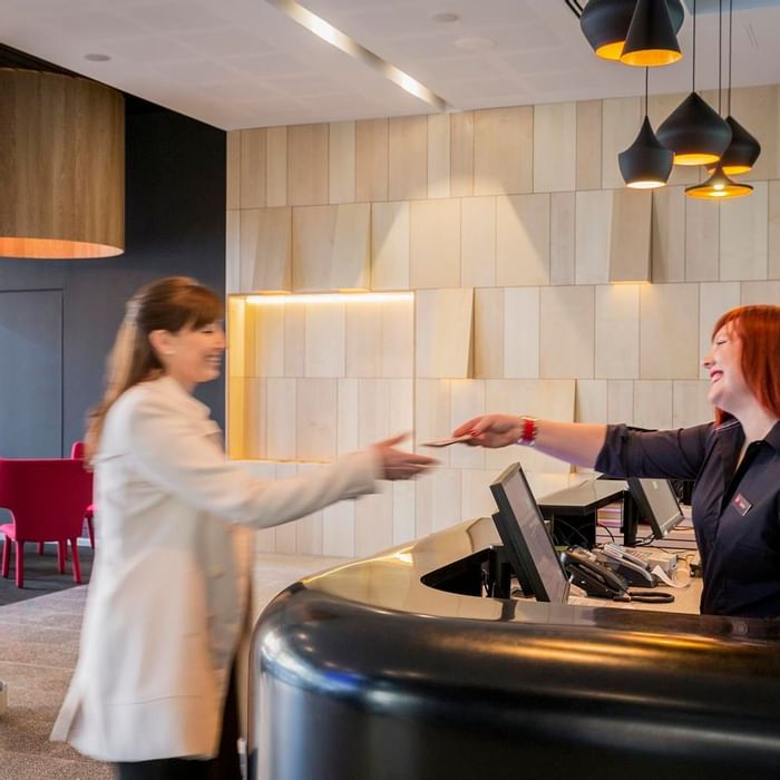 Guest happily receiving a key card from a smiling receptionist at Ibis Adelaide