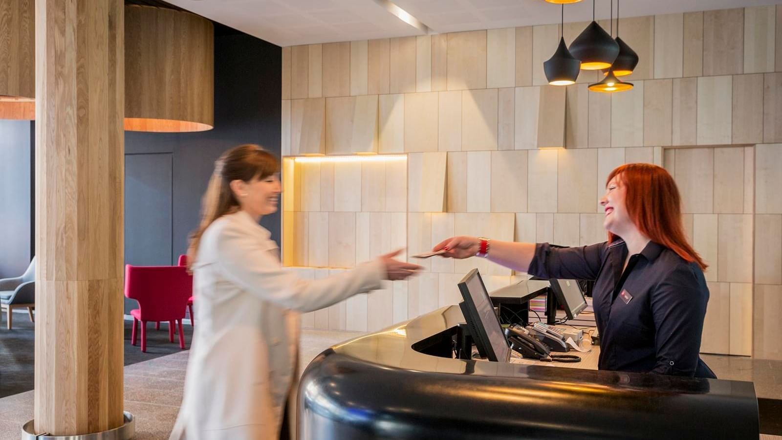 Guest happily receiving a key card from a smiling receptionist at Ibis Adelaide