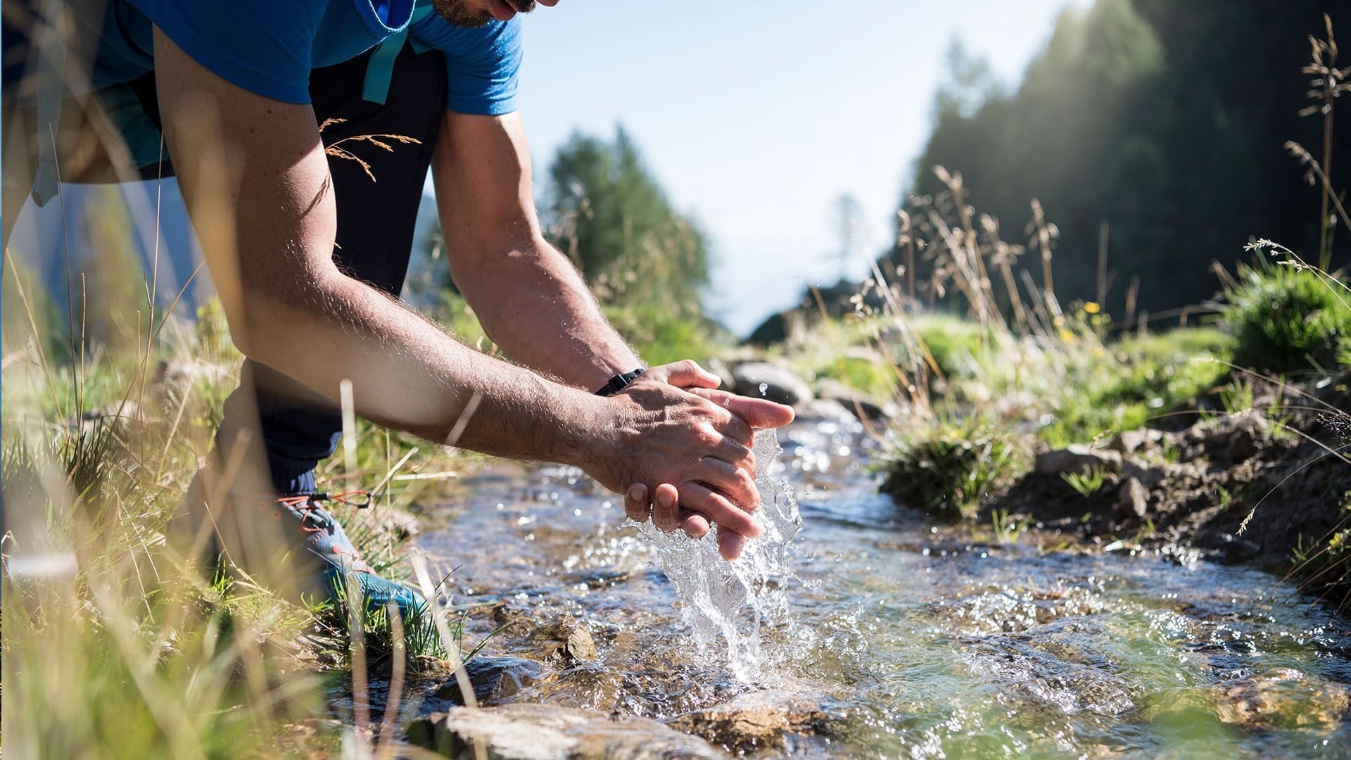 A hiker washing hands in a stream near Falkensteiner Hotels