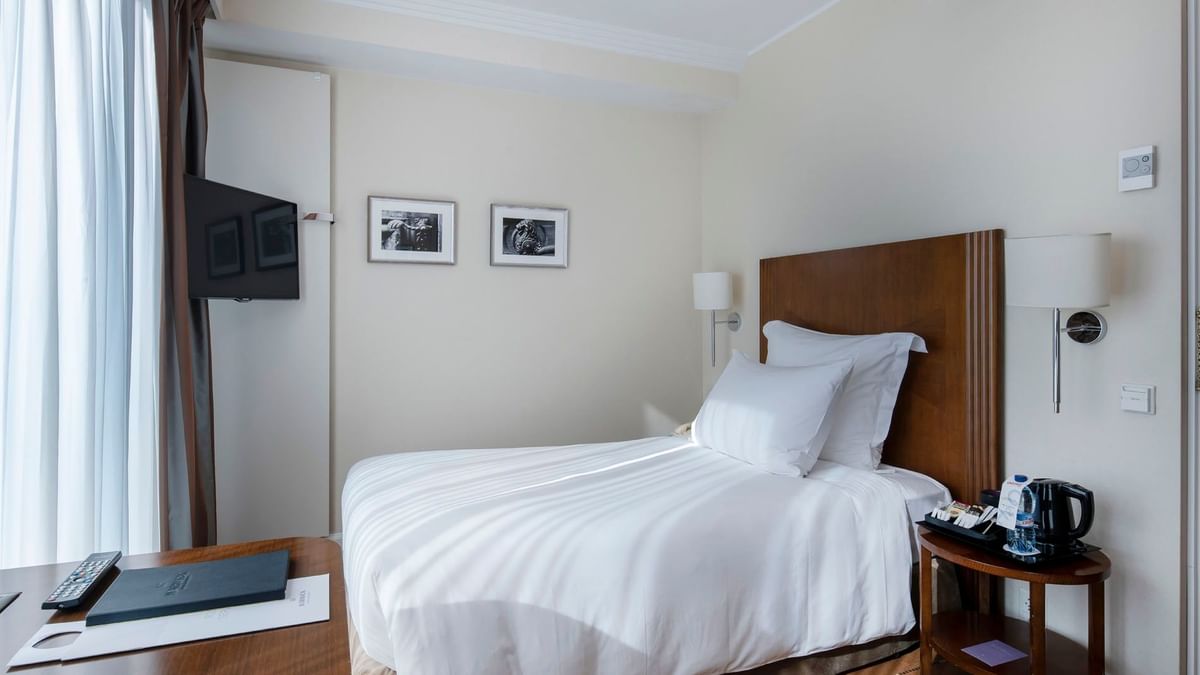 Cozy bed by a side table under a wall lamp with a TV by a window in Classic Single Room at Warwick Geneva