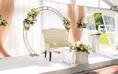 Tufted white loveseat under floral gold arch on draped stage in Spencer Meadows Pavilion at Spencer Hotel