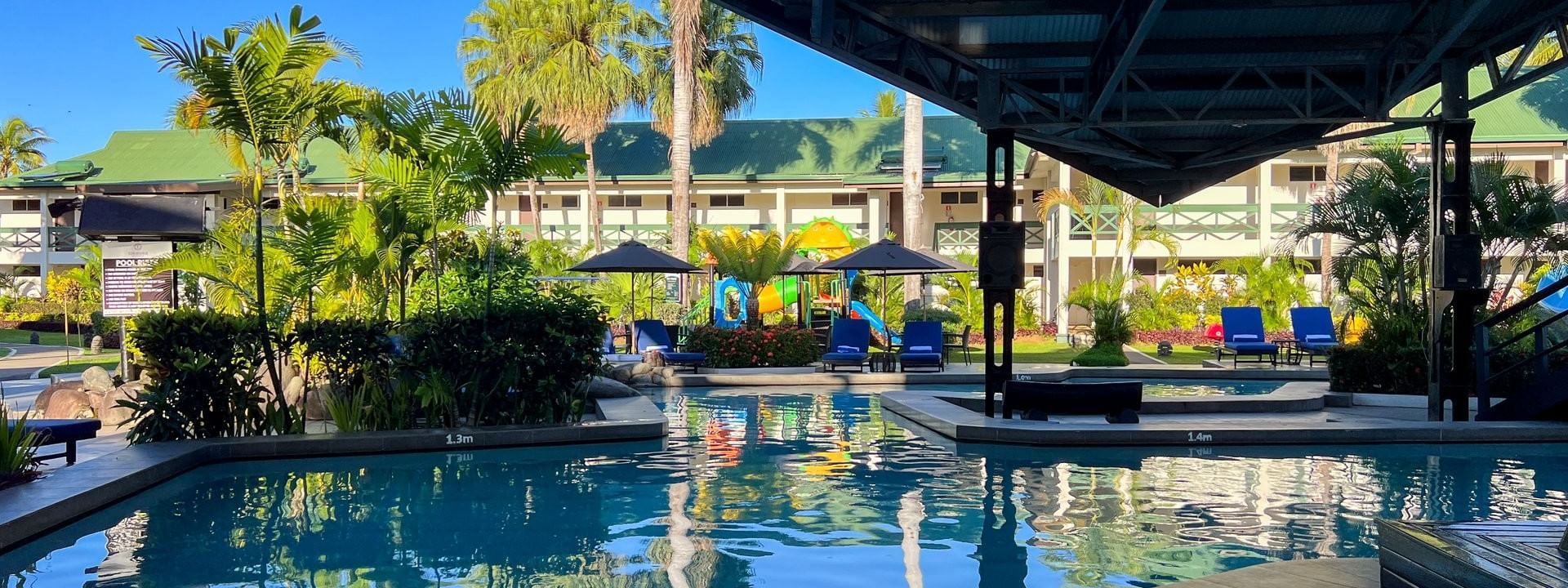Swimming pool with clear water and lounge chairs under palm trees at Tokatoka Resort in Nadi