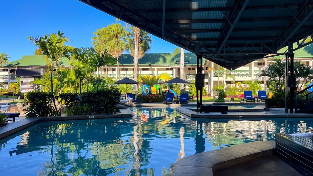 Swimming pool with clear water and lounge chairs under palm trees at Tokatoka Resort in Nadi.