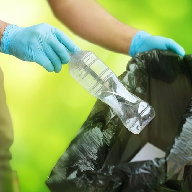 Person putting a plastic bottle into a trash bag at Imperial Lexis 5 star hotel in Kuala Lumpur