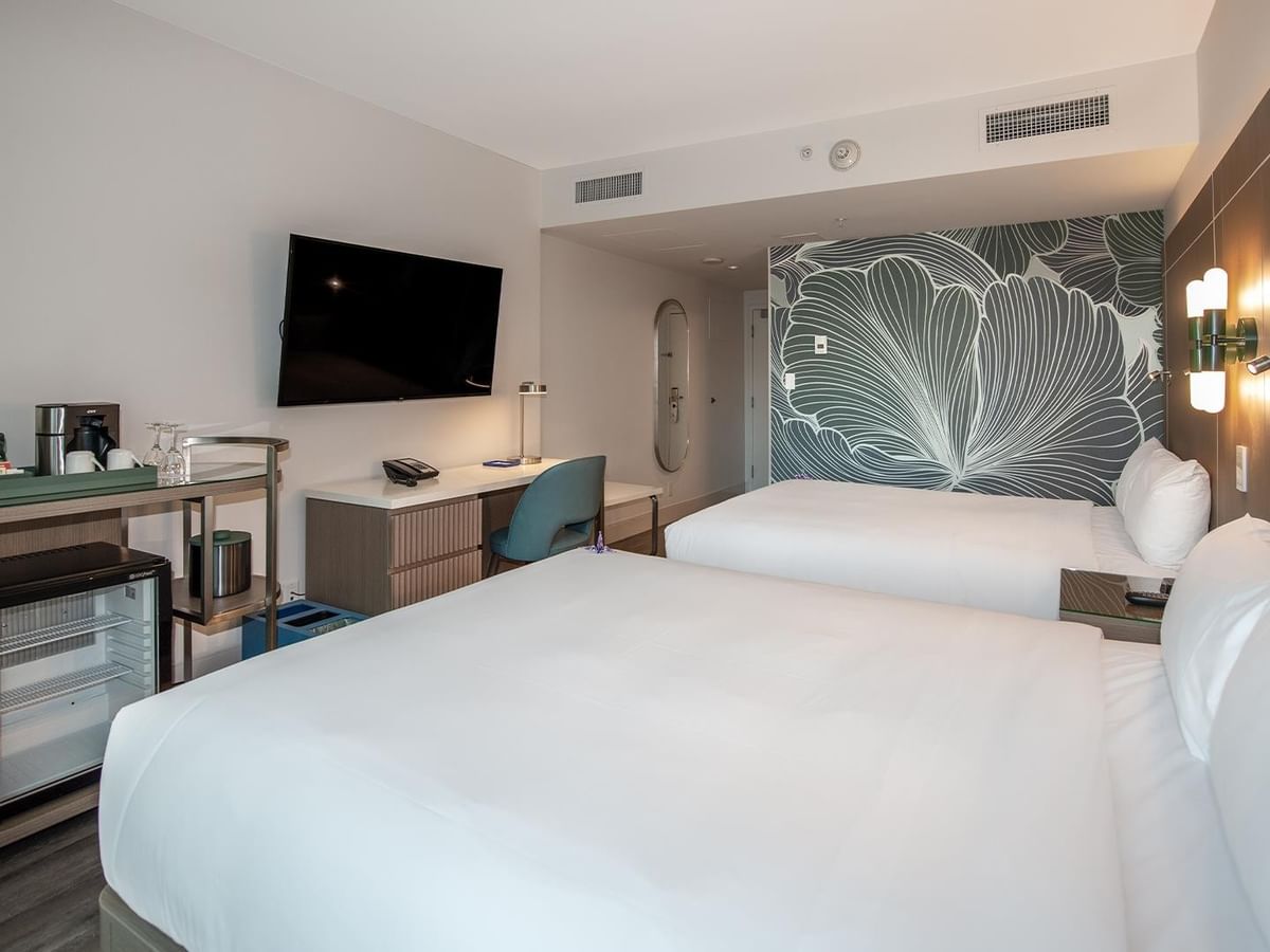 Two queen beds with a desk and flat-screen TV in a room.