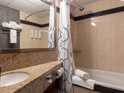 Bathroom with bathtub, sink, mirror, and towels at Carriage House Hotel & Conference Centre